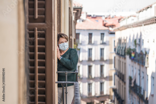 mature woman with face mask sad and scared at home balcony during covid19 pandemic lockdown looking to the street confused and depressed in senior people virus fear concept © TheVisualsYouNeed