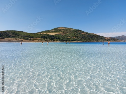 People in the distance in the shallow blue clear water of Lake Salda in Turkey with a mountain in the background on a sunny day. The best sights of Turkey. Turkish Maldives.. High quality photo