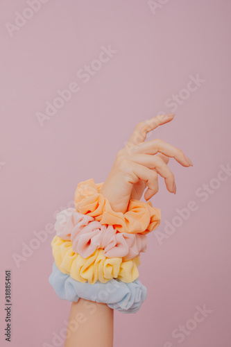 female hand holding many scrunchies . Female hand isolated on pink background