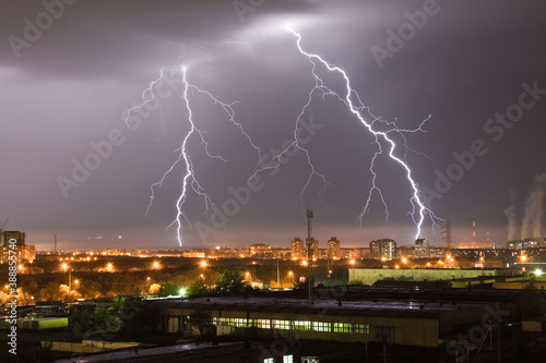 Powerful flash lightning hitting the city at night over dark gray sky. A strong lightning strike over hits the ground  illuminating the industrial area around.