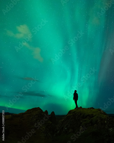 An adventure solo traveler posing with the beautiful northern lights also known as aurora borealis in the background. A breathtaking nature of Iceland as nordic country