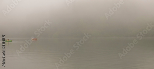 Two boats are sailing to fish in a mystic foggy lake.