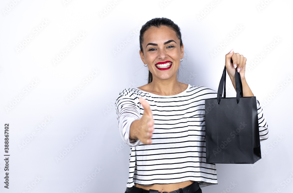 Young beautiful woman holding a black shopping bag smiling friendly offering handshake as greeting and welcoming. Black Friday Young beautiful woman holding a black shopping bag smiling friendly offering handshake as greeting and welcoming. Black Friday