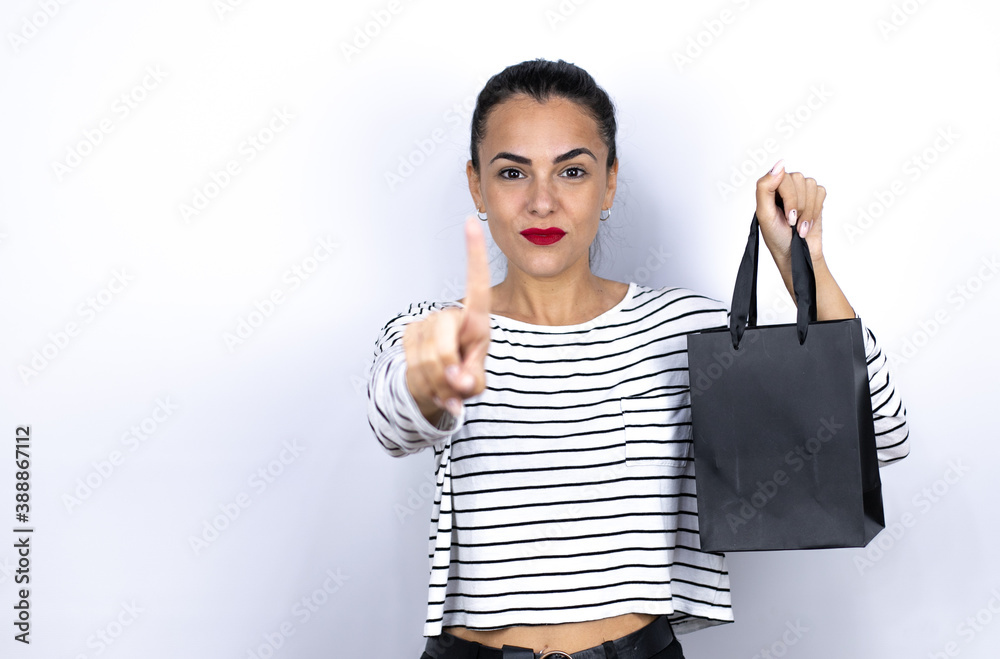 Young beautiful woman holding a black shopping bag showing and pointing up with fingers number one while is serious. Black Friday Young beautiful woman holding a black shopping bag showing and pointing up with fingers number one while is serious. Black Friday
