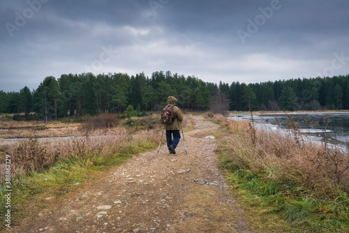 A man with a backpack and ski poles is engaged in Nordic walking on the lake. © Anatoliy