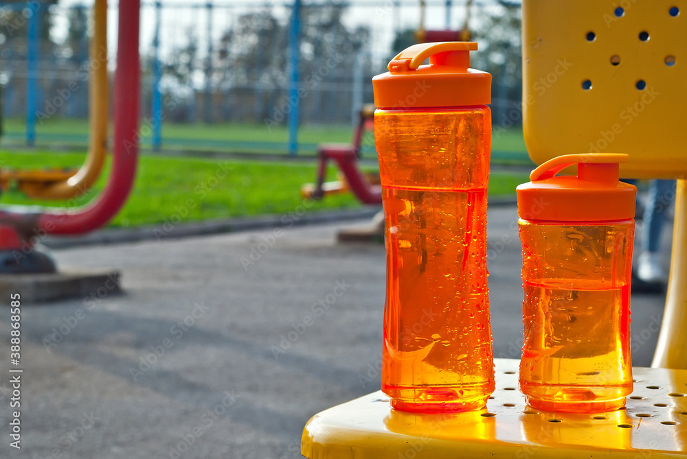 Orange bottle with water on the background of sports equipment. Yellow and red street simulators.