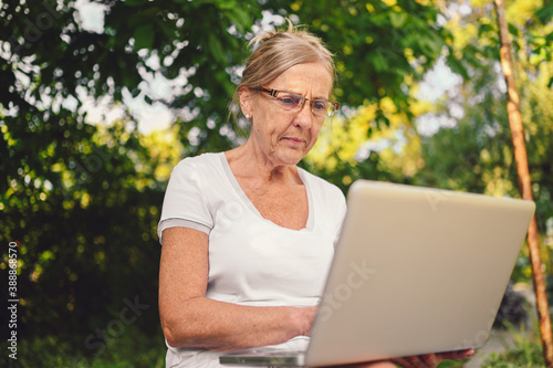 Happy senior old woman working online with laptop computer outdoor in garden © Алина Троева