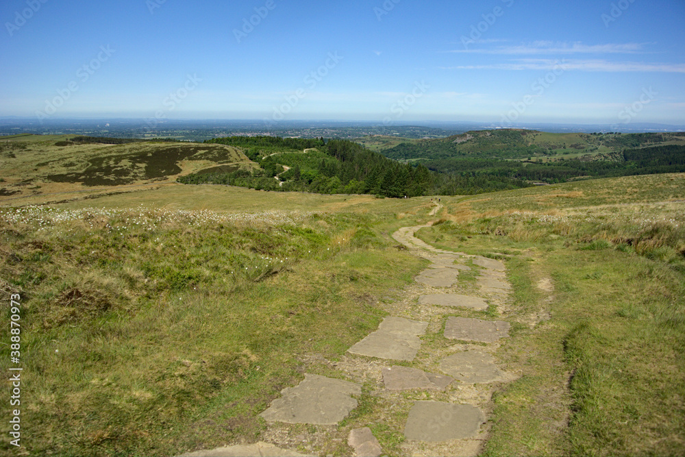 An ancient Celtic stone slab path leading to a rural landscape under a clear blue sky