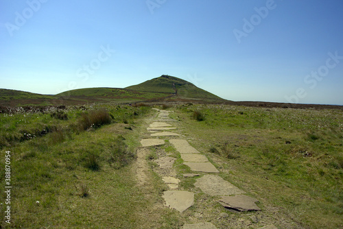 An ancient Celtic stone slab path leading to a distant hill under a clear blue sky