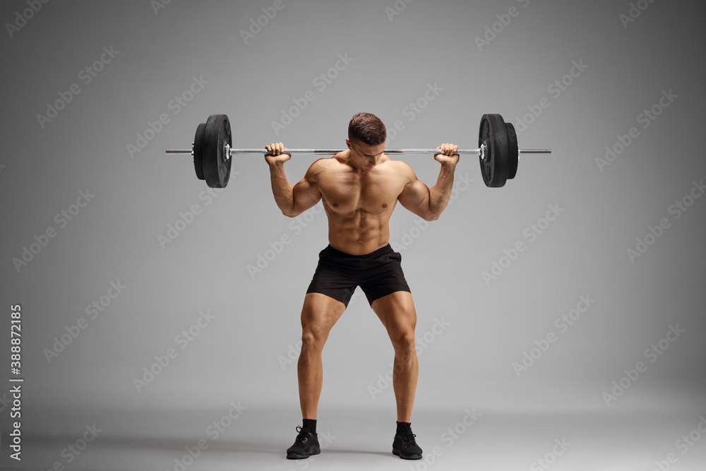 Topless bodybuilder lifting weights on a gray background