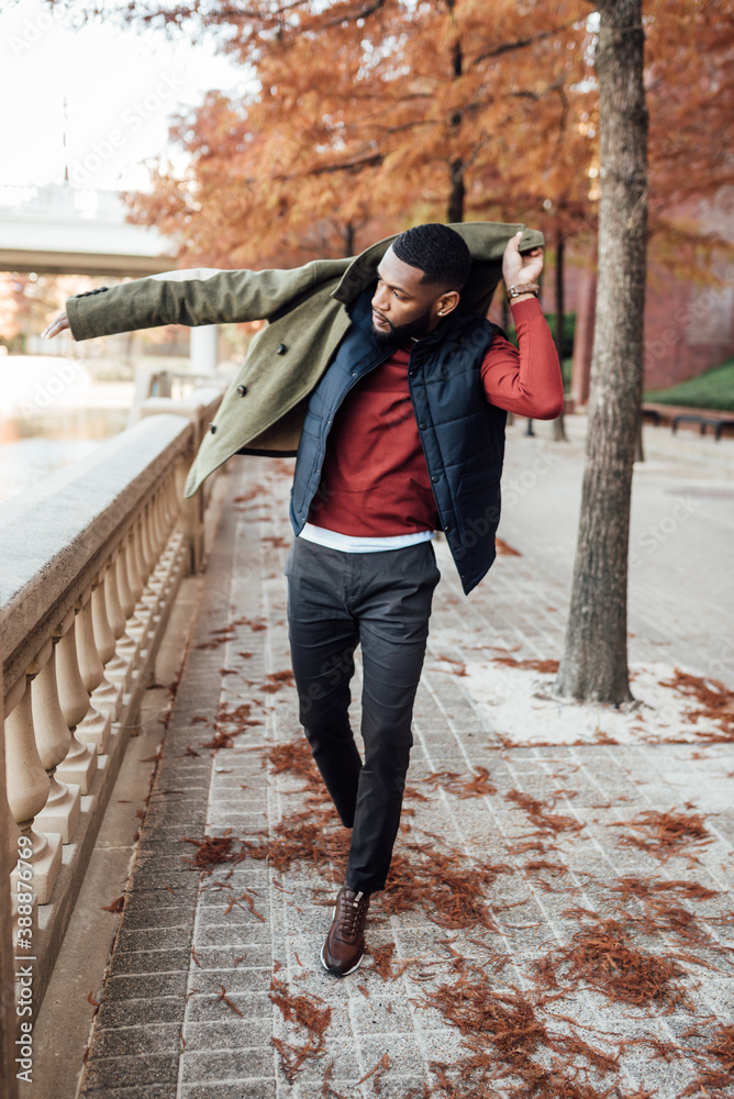 Man wearing blue vest and green jacket walking in park
