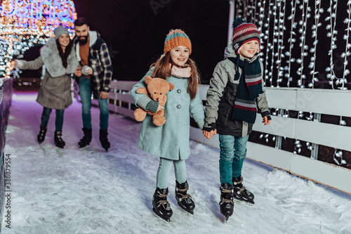 Happy young family having fun and enjoying in beautiful winter night at frozen skating park.