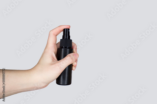 A white hand holds a black spray on a gray background