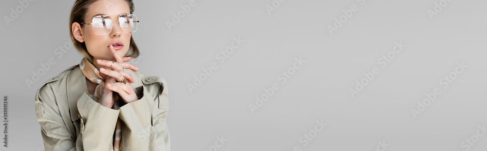 trendy woman in glasses, trench coat and scarf posing on grey, banner - obrazy, fototapety, plakaty 