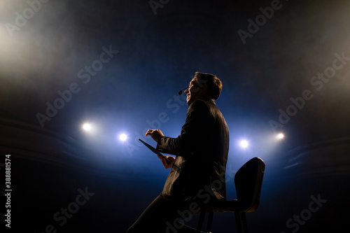 Portrait of men speaking through a microphone in dark conference hall. Man talks into microphones at press conference. Profile of young male politician speaking passionately from tribune