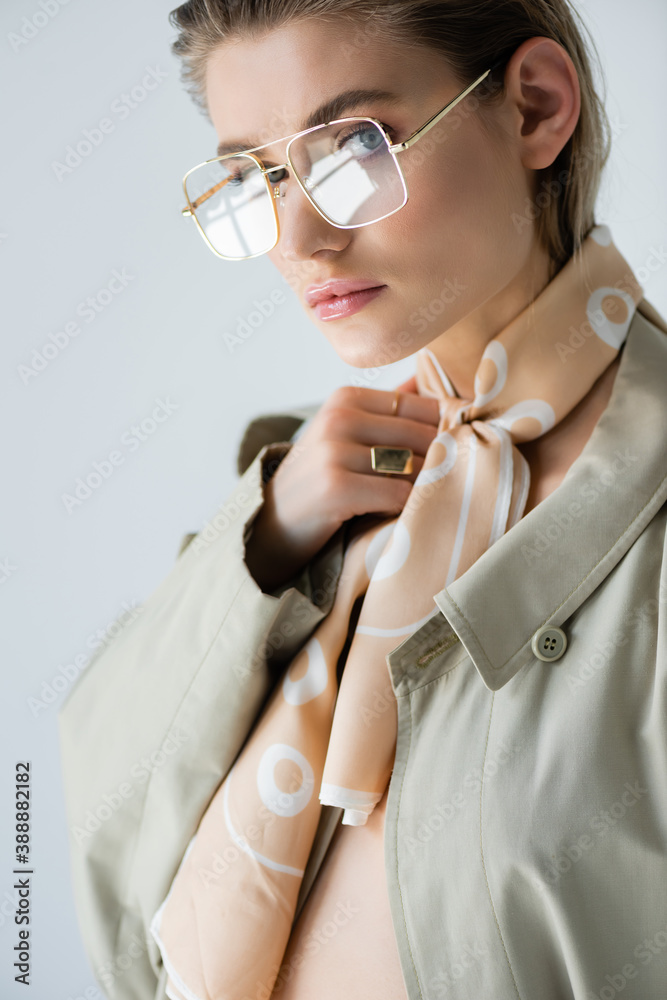 Φωτογραφία trendy woman in glasses, trench coat and scarf looking at camera isolated on whi