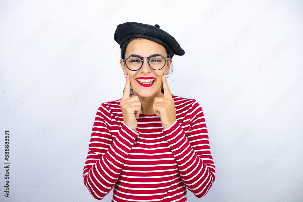 Young beautiful brunette woman wearing french beret and glasses over white background smiling confident showing and pointing with fingers teeth and mouth Young beautiful brunette woman wearing french beret and glasses over white background smiling confident showing and pointing with fingers teeth and mouth