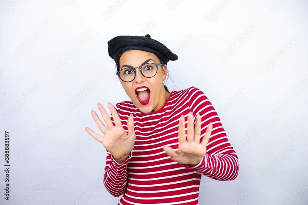 Young beautiful brunette woman wearing french beret and glasses over white background afraid and terrified with fear expression stop gesture with hands, shouting in shock. Panic concept. Young beautiful brunette woman wearing french beret and glasses over white background afraid and terrified with fear expression stop gesture with hands, shouting in shock. Panic concept.
