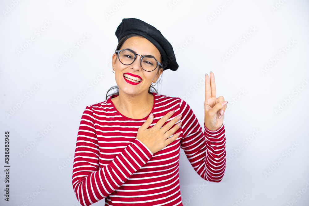Young beautiful brunette woman wearing french beret and glasses over white background smiling swearing with hand on chest and fingers up, making a loyalty promise oath Young beautiful brunette woman wearing french beret and glasses over white background smiling swearing with hand on chest and fingers up, making a loyalty promise oath