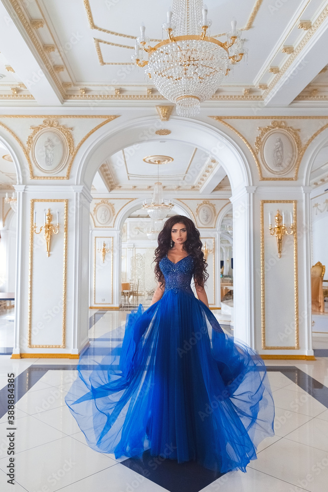 Sensual brunette girl in a blue evening dress on the background of a beautiful classic interior