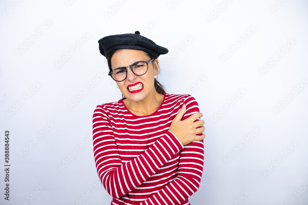 Young beautiful brunette woman wearing french beret and glasses over white background with pain on her shoulder and a painful expression Young beautiful brunette woman wearing french beret and glasses over white background with pain on her shoulder and a painful expression