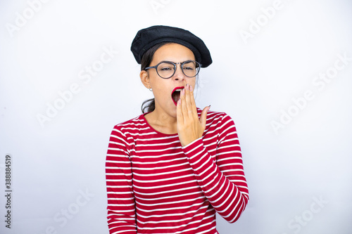 Young beautiful brunette woman wearing french beret and glasses over white background bored yawning tired covering mouth with hand. Restless and sleepiness.