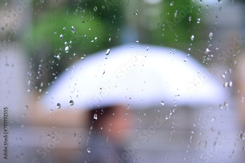 ガラスについた雨粒と雨傘をさす人