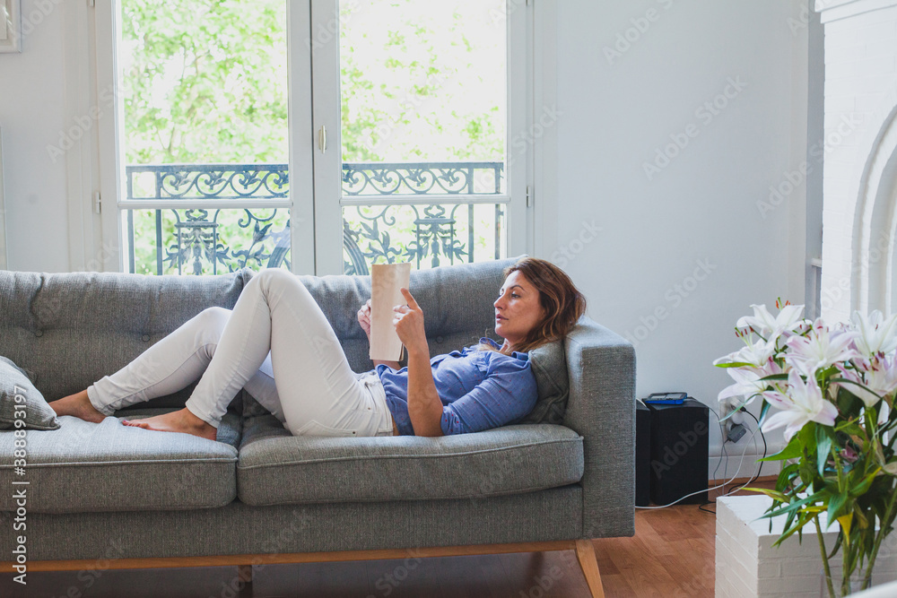 woman reading at home while lying down on the couch woman reading at home while lying down on the couch