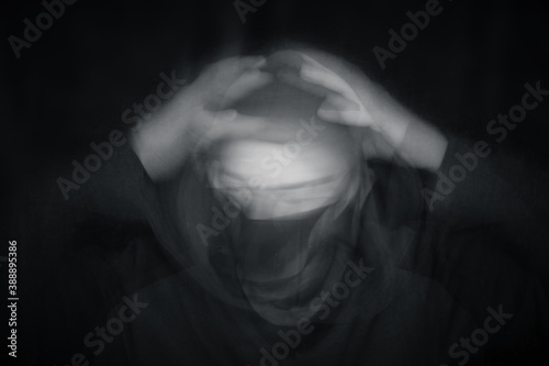 A double exposure of a blurred, hooded man wearing a mask.