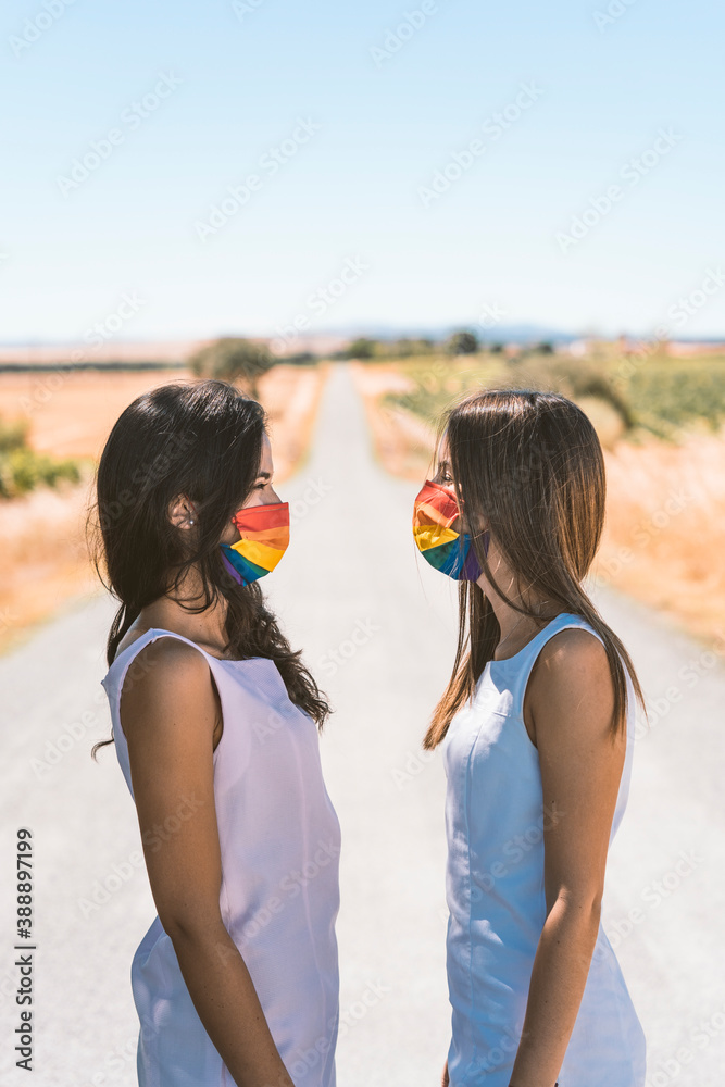 Women with rainbow face mask looking at each other while standing on road Women with rainbow face mask looking at each other while standing on road