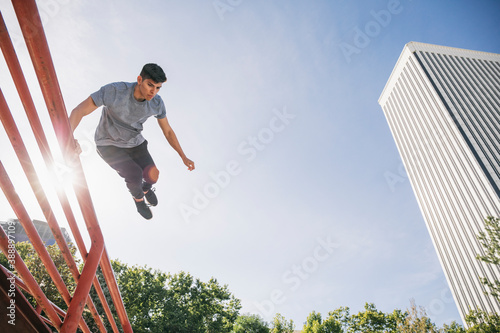 Young man jumping over railing performing parkour against clear sky in city photo