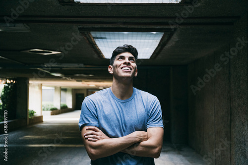 Thoughtful smiling young man with arms crossed standing in basement photo