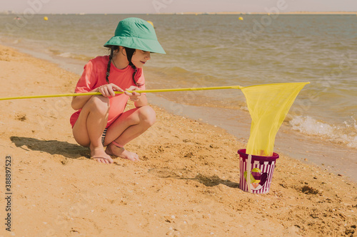 Girl with fishing net crouching at beach during sunny day photo