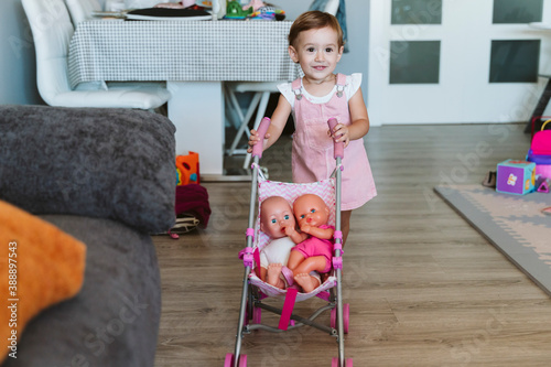 Baby girl playing with baby stroller and doll at home