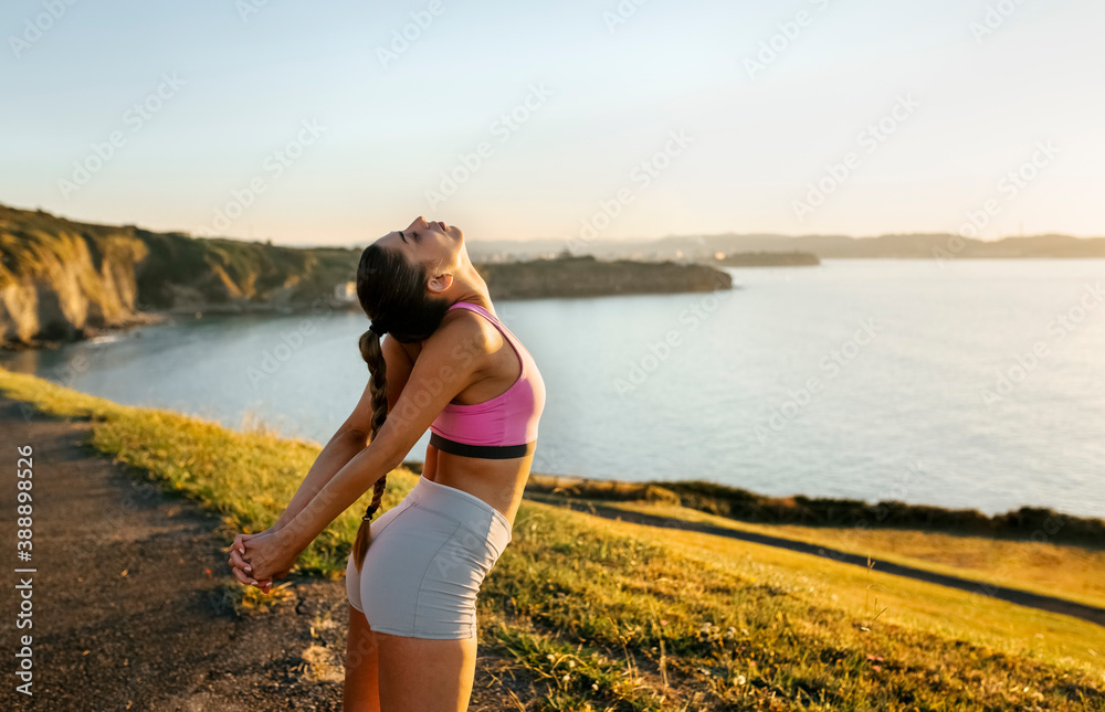 Young woman stretching hands while standing on cliff against clear sky during sunset Young woman stretching hands while standing on cliff against clear sky during sunset