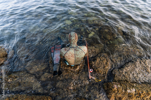 Man wearing wetsuit with flipper and harpoon sitting on rocks in sea