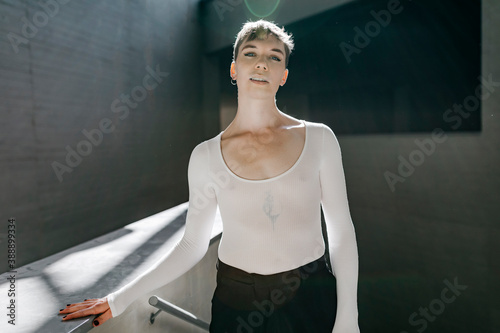 Non-binary young man wearing white leotard standing in basement photo