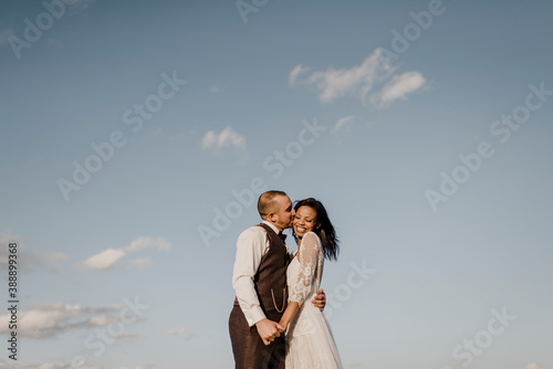 Bridegroom kissing bride on cheek during sunny day