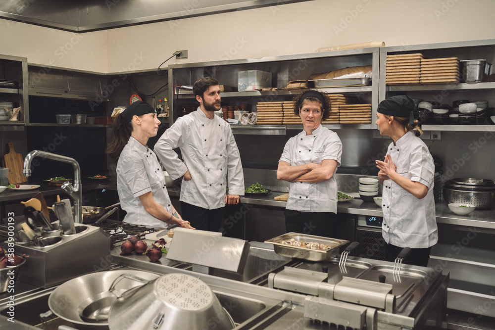 Female chef talking to coworkers in commercial kitchen Female chef talking to coworkers in commercial kitchen