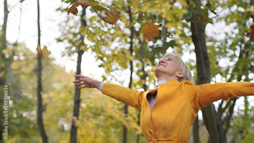 Happy caucasian woman trowing yellow autumn leaves in the park and spinning around. High quality photo