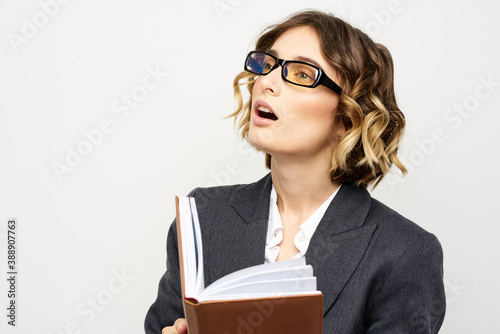 Woman at work with book in hand light background classic suit glasses head