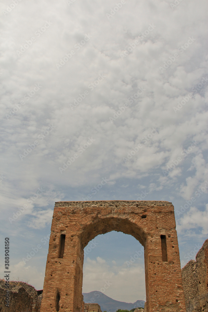 View of Mount Vesuvius through an archway against a cloudy sky in Pompeii, Italy. No people, space for copy.