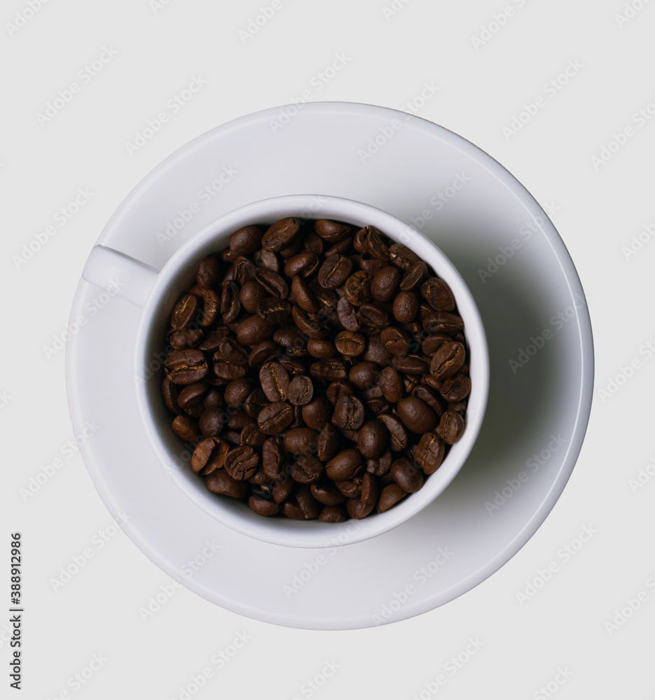 grains of black coffee in a white mug on a white saucer top view isolated grains of black coffee in a white mug on a white saucer top view isolated