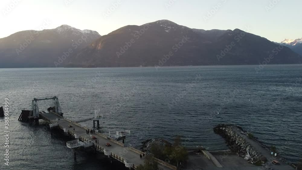 Fly over dock with people walking around near water and mountains on background Fly over dock with people walking around near water and mountains on background
