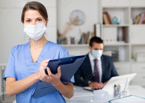 Portrait of nurse in protective medical mask with folder of documents at clinic office
