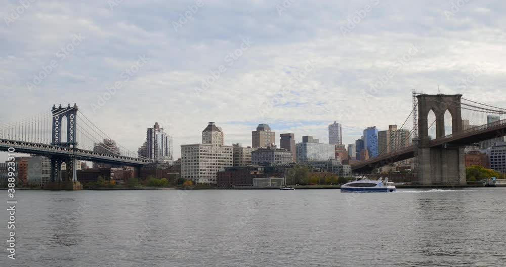 View of the Brooklyn Bridge and the Manhattan Bridge from the Lower East Side of Manhattan. We see a ferry pass by as we look towards Brooklyn. View of the Brooklyn Bridge and the Manhattan Bridge from the Lower East Side of Manhattan. We see a ferry pass by as we look towards Brooklyn.