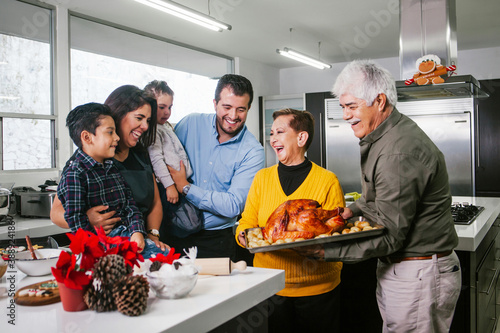 Latin family laughing at the kitchen with Christmas turkey on the oven plate in Mexico photo