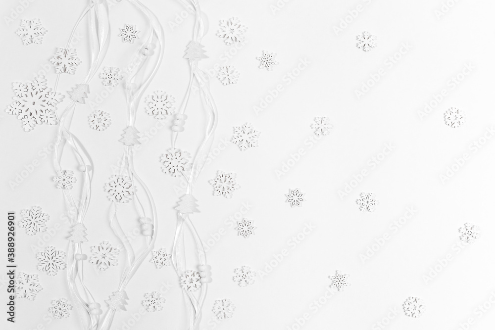 Christmas white background made of white wooden snowflakes and small Christmas trees and round beads on narrow ribbons.