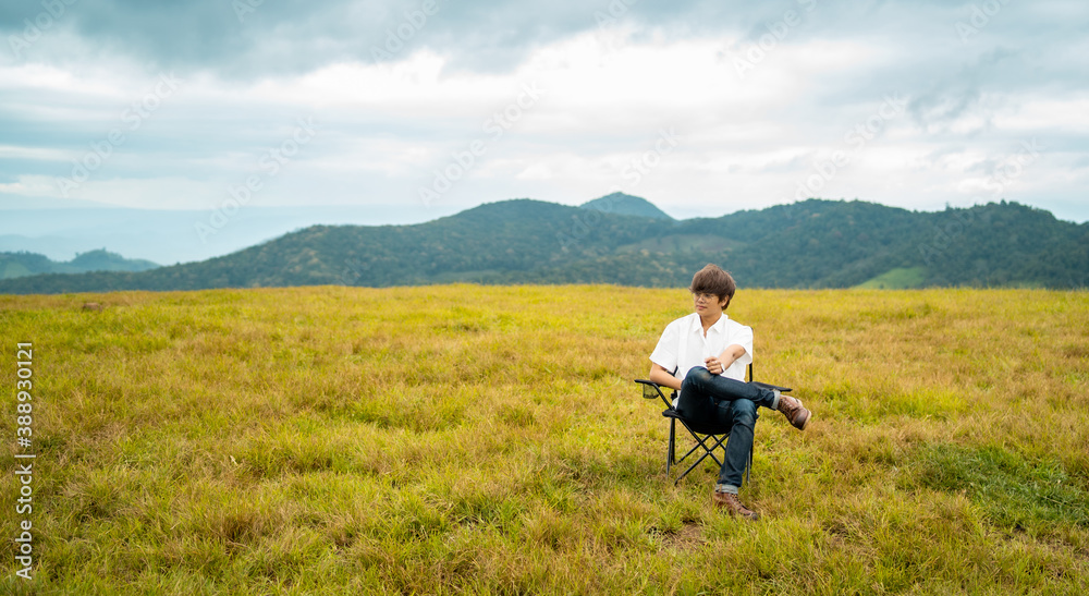 Happy young Asian man sitting alone on outdoor chair relaxing in beautiful nature of the mountain grass field in autumn day. Loneliness handsome guy enjoy with outdoor lifestyle on holiday vacation Happy young Asian man sitting alone on outdoor chair relaxing in beautiful nature of the mountain grass field in autumn day. Loneliness handsome guy enjoy with outdoor lifestyle on holiday vacation