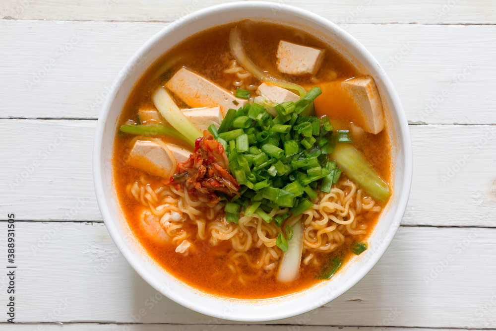 Top view a bowl of Korean noodle soup or Ramen kimchi with tofu, egg, vegetable and garnish with spring onion and Kimchi on white wooden table Top view a bowl of Korean noodle soup or Ramen kimchi with tofu, egg, vegetable and garnish with spring onion and Kimchi on white wooden table